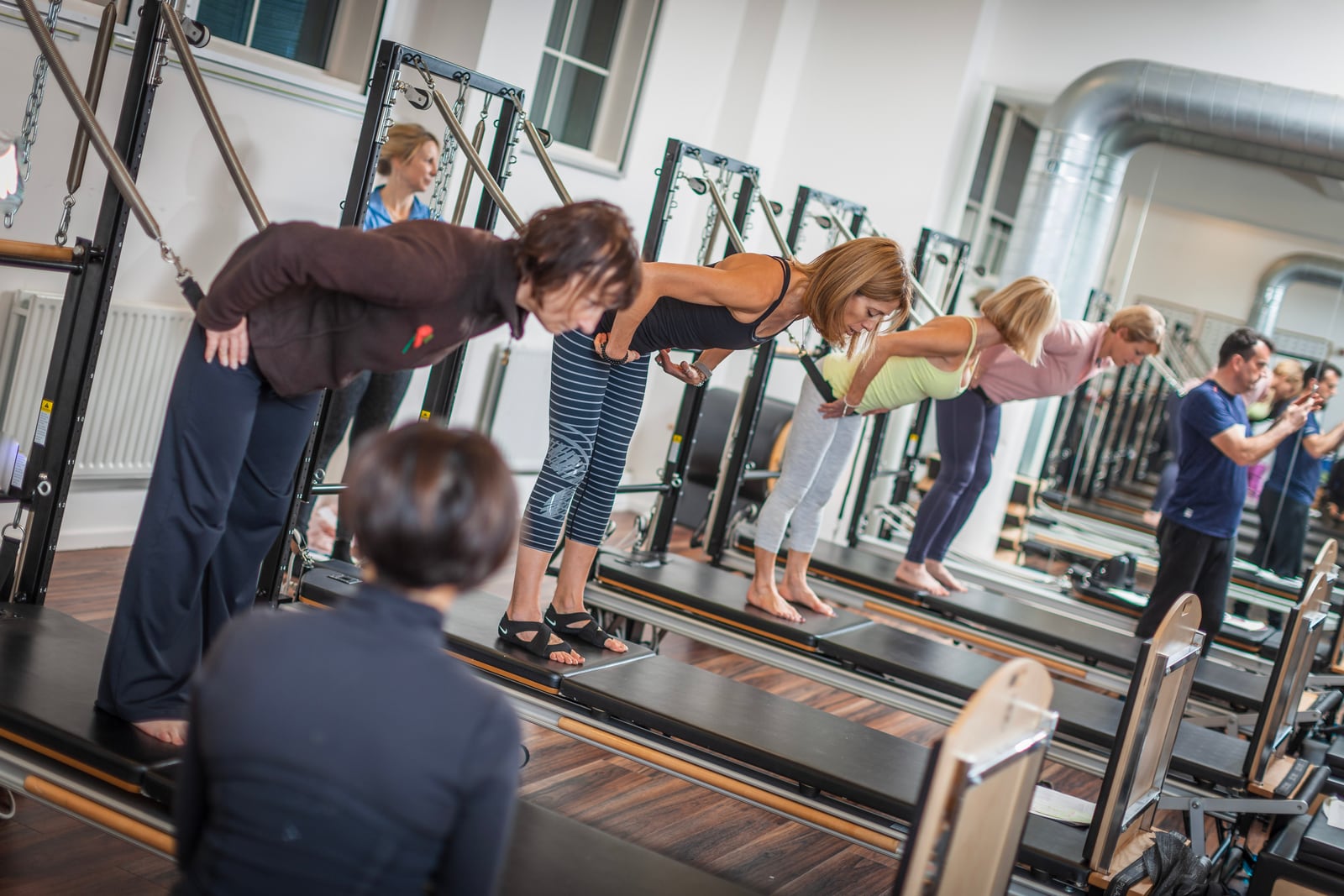 Group practising standing exercises with spring resistance on Pilates apparatus