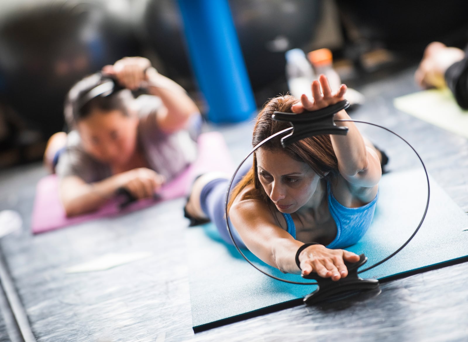 Participants practising a controlled mat exercise with Pilates rings